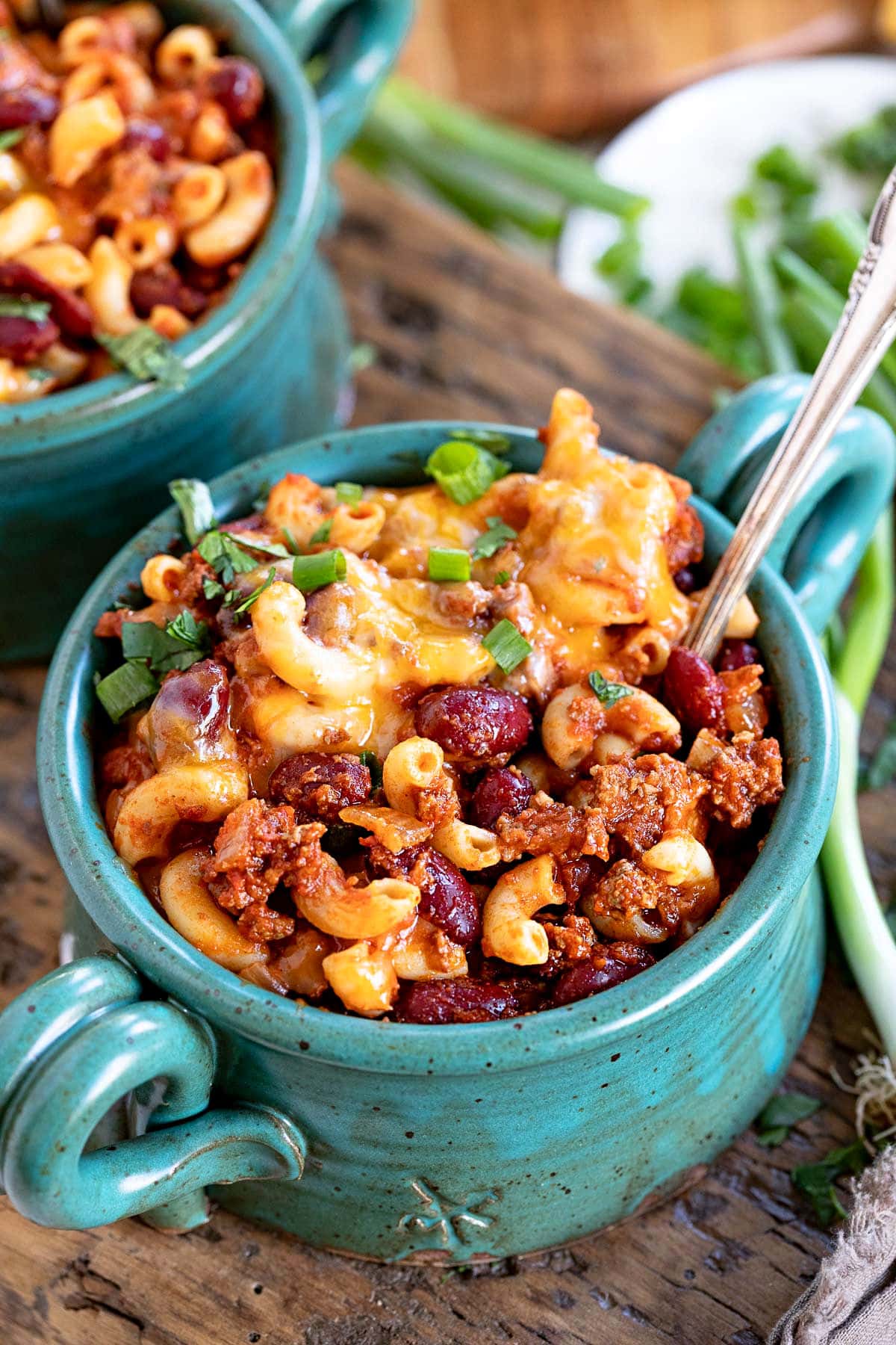 teal bowl filled with chili mac and topped with shredded cheese and sliced green onions.