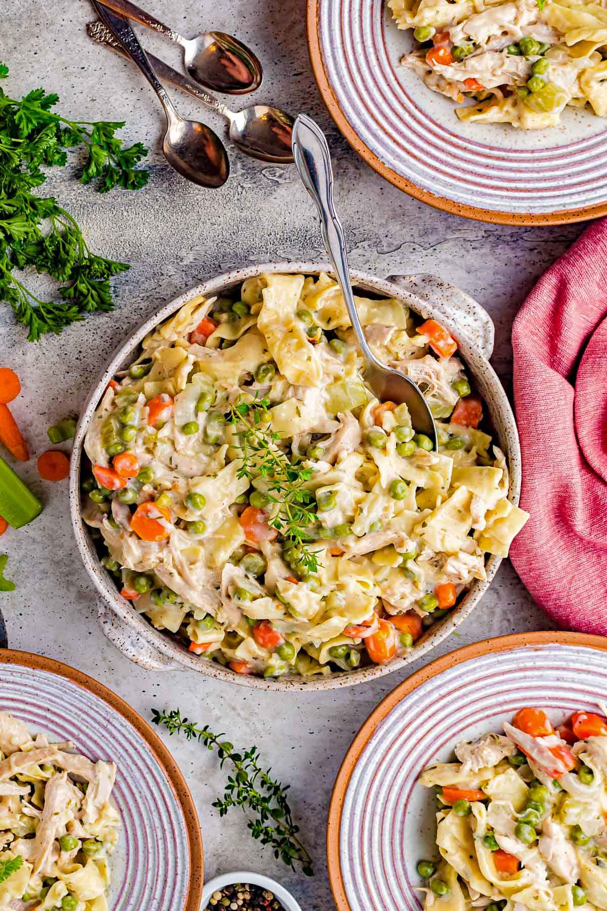 top down view of large serving bowl with chicken noodles recipe and three plates with servings already dished out. 