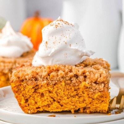 piece of pumpkin coffee cake sitting on stack of white plates topped with whipped cream