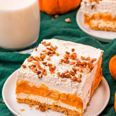 top down look at four layer pumpkin dessert sitting on white plate topped with pecans and pumpkin pie spice. glass of milk in background.