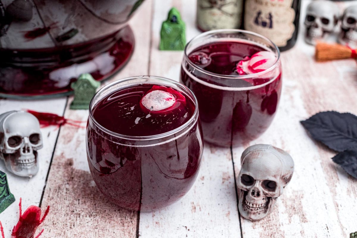 two glasses filled with dark red punch and floating skull ice cubes.