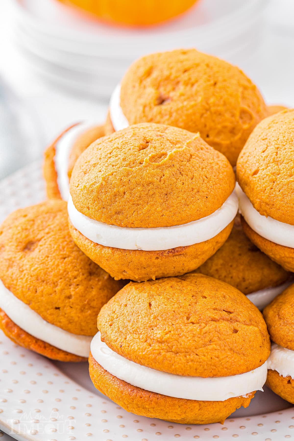 a dozen pumpkin whoopie pies on a white plate piled high.