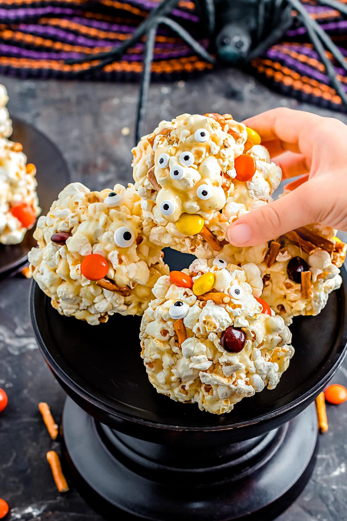 hand picking up a halloween popcorn ball of a tall black cake stand.