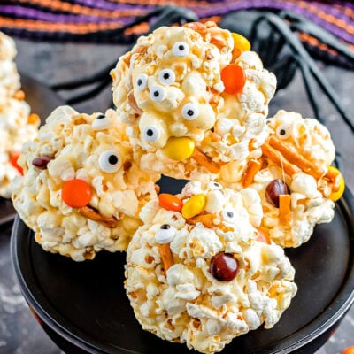 popcorn balls decorated for halloween with pretzels and candies sitting on black cake stand.