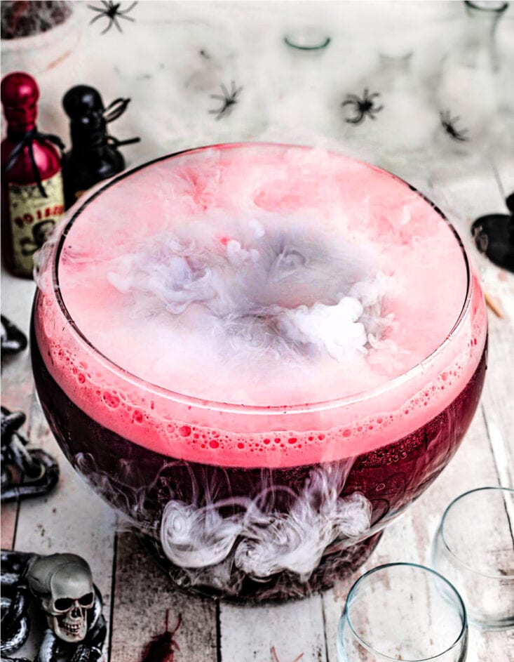 halloween punch that is dark red served in a large glass punch bowl with fog on top created by dry ice.