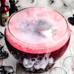 halloween punch that is dark red served in a large glass punch bowl with fog on top created by dry ice.