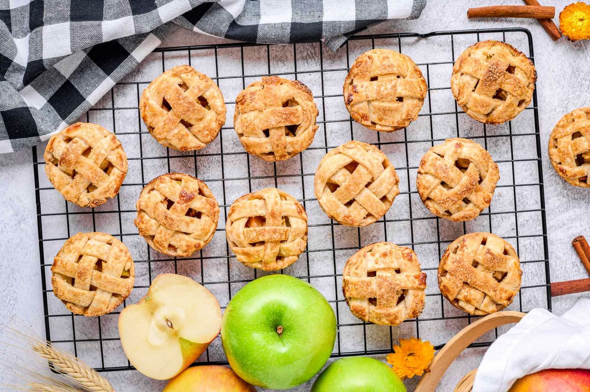 apple pies made in a muffin pan cooling on black wire rack.