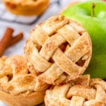 three mini apple pies resting near a green granny smith apple.