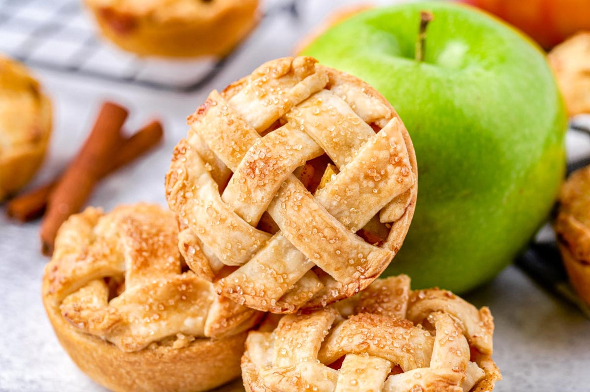 three mini apple pies resting near a green granny smith apple.