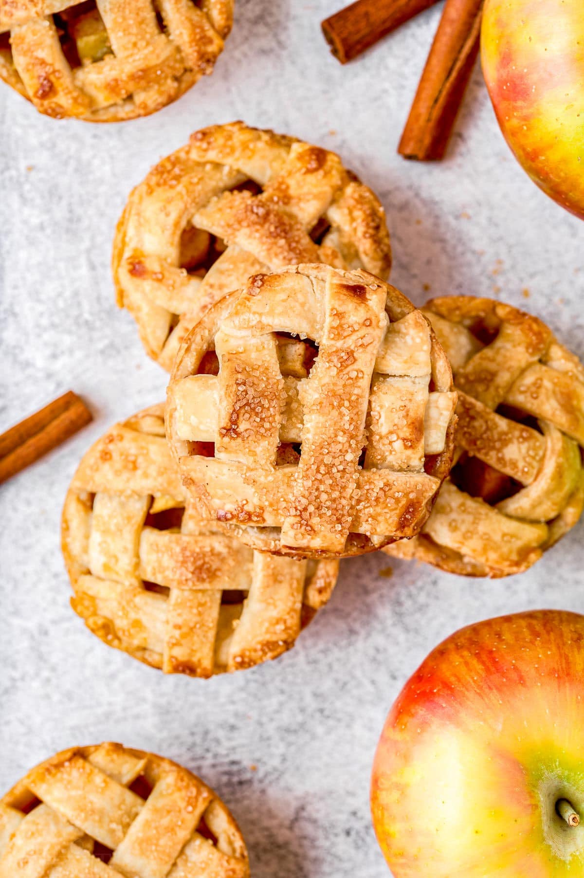 four mini apple pies stacked in a pyramid with cinnamon sticks and apples around them.
