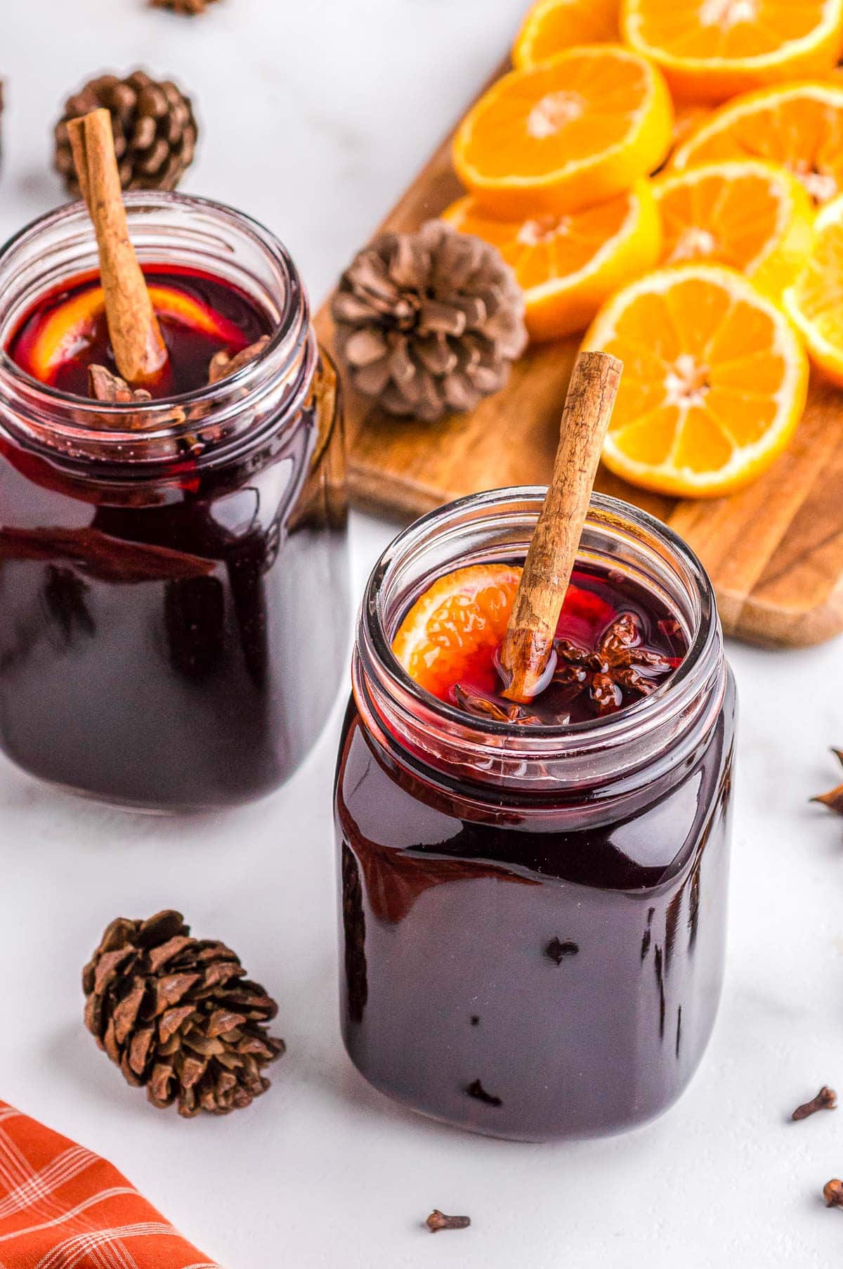 two large glass mugs of mulled wine garnished with spices and orange slices. 