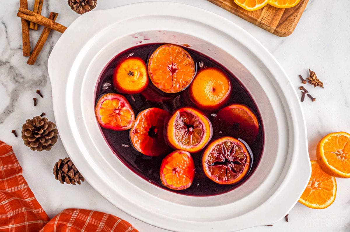 top down look at mulled wine crockpot version in white crockpot. Orange slices and cinnamon sticks sitting with the wine.