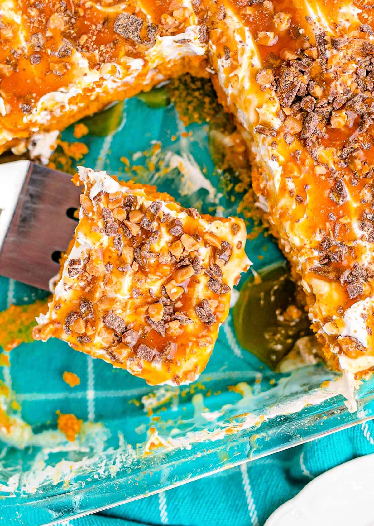 top down look at pumpkin poke cake topped with cool whip, caramel and toffee bits. several pieces removed and one piece on server.