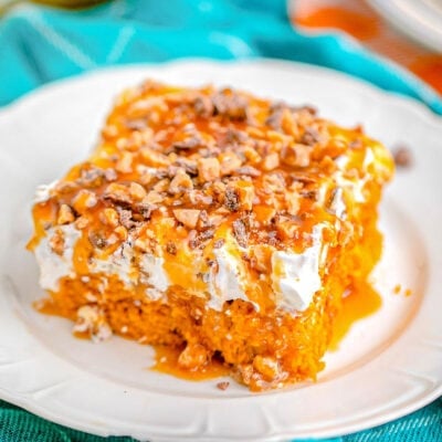 pumpkin cake sitting on white plate with bright blue napkin in the background. topped with cool whip and heath toffee bits.
