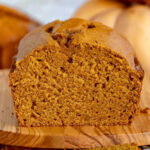 loaf of pumpkin bread sitting on olive board with one piece sliced off.