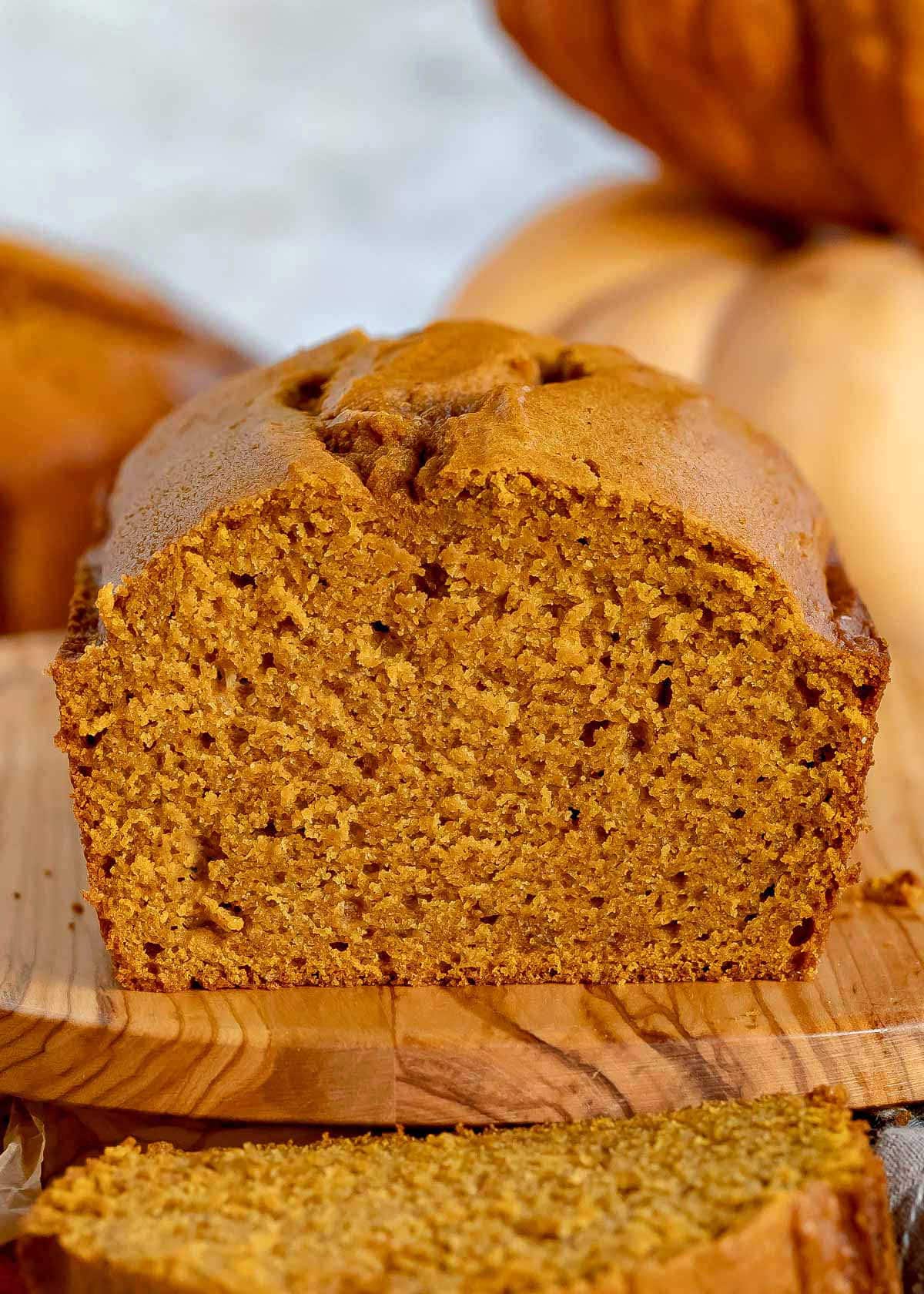 loaf of pumpkin bread sitting on olive board with one piece sliced off.