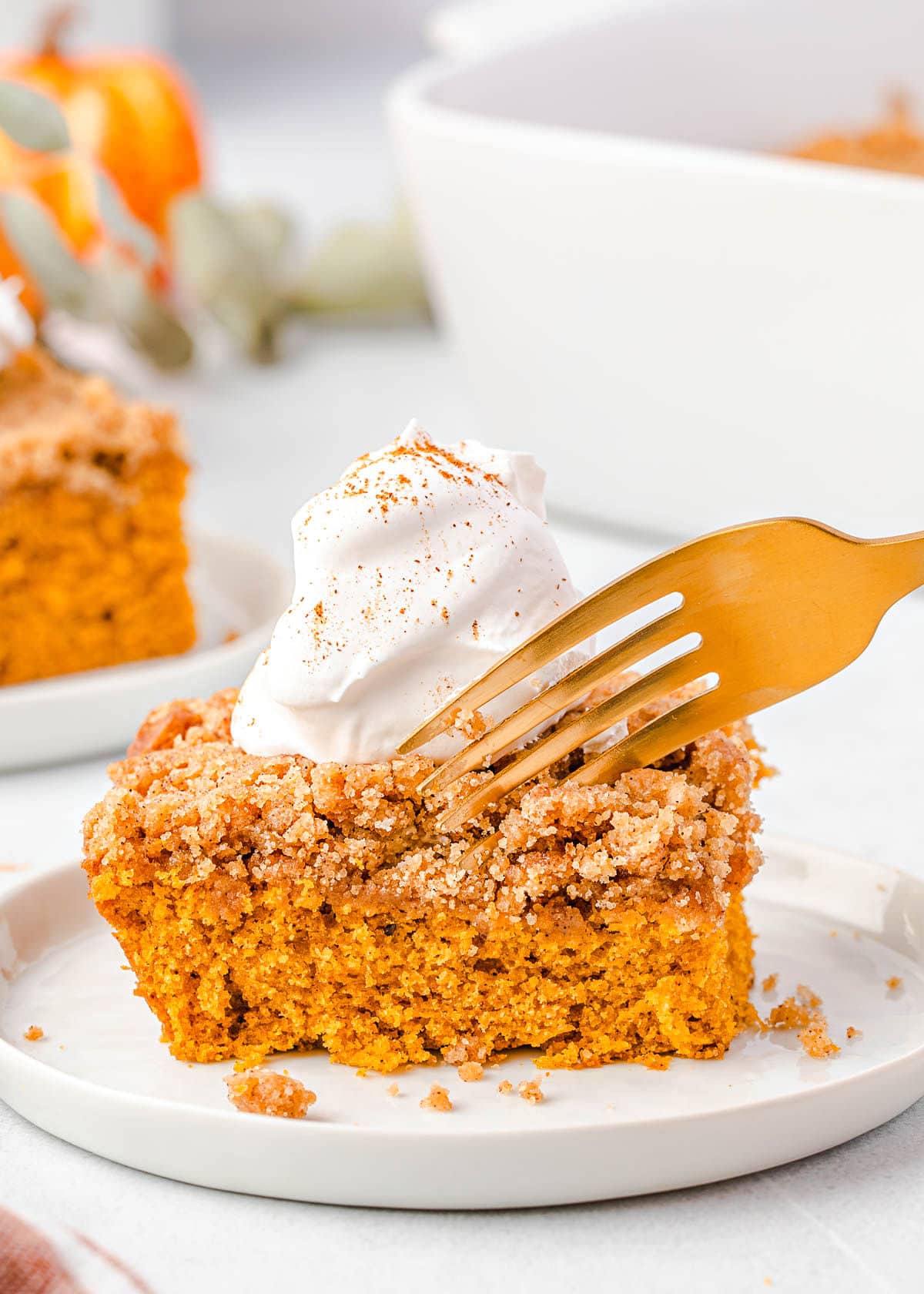 fork getting ready to take a bite of pumpkin cake with whipped cream on top.