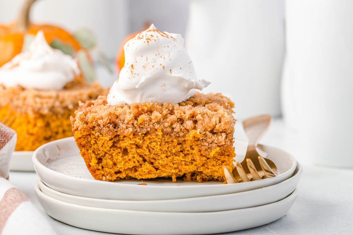 pumpkin coffee cake topped with whipped cream and a dusting of pumpkin pie spice sitting on 3 white stacked plates.