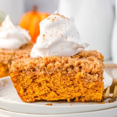 piece of pumpkin coffee cake sitting on stack of white plates topped with whipped cream