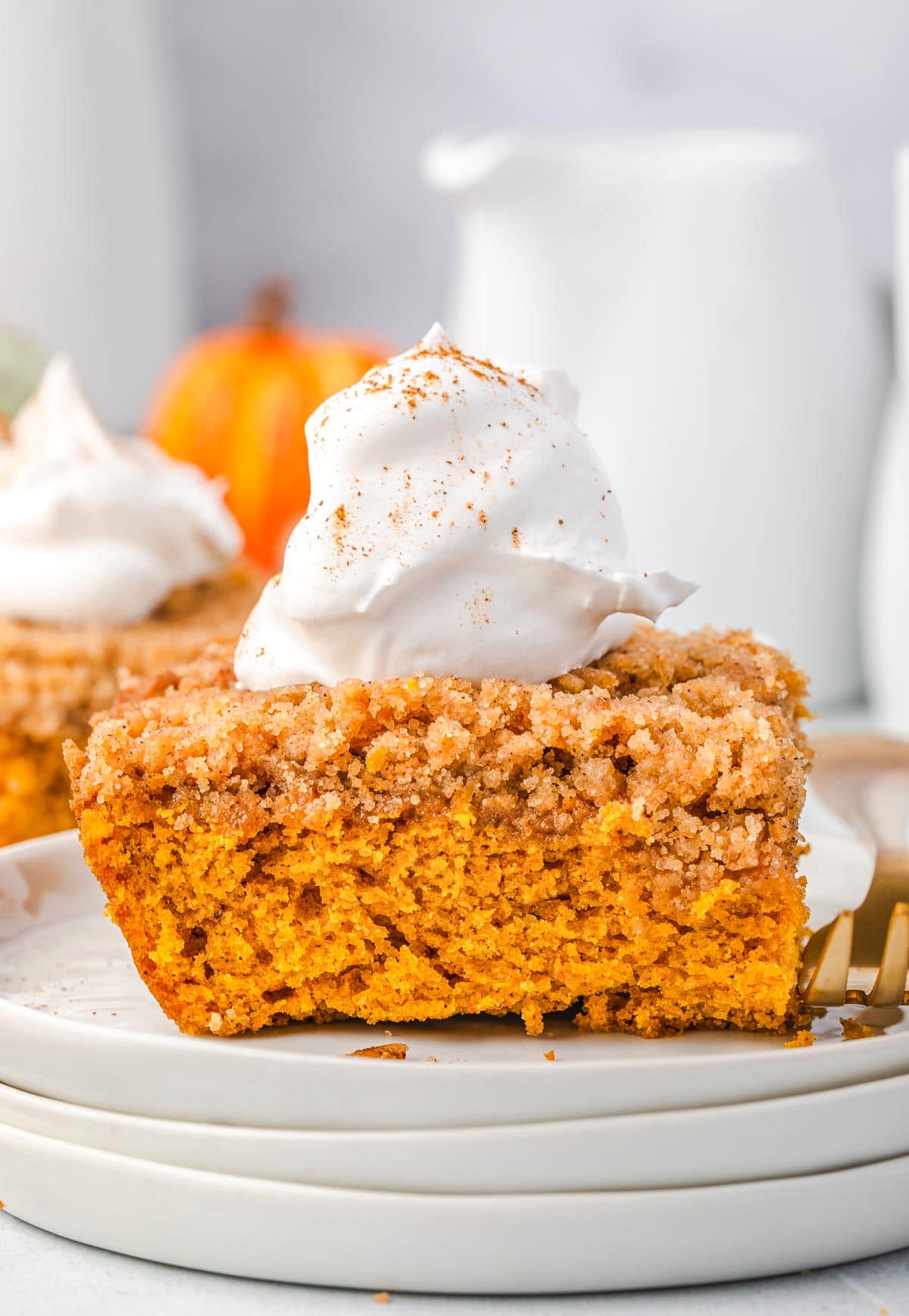 piece of pumpkin coffee cake sitting on stack of white plates topped with whipped cream