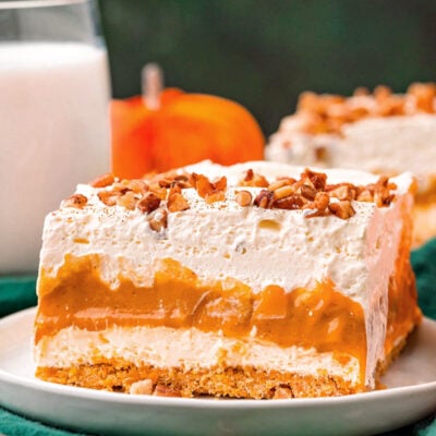 four layer pumpkin dessert sitting on white plate topped with pecans and pumpkin pie spice.