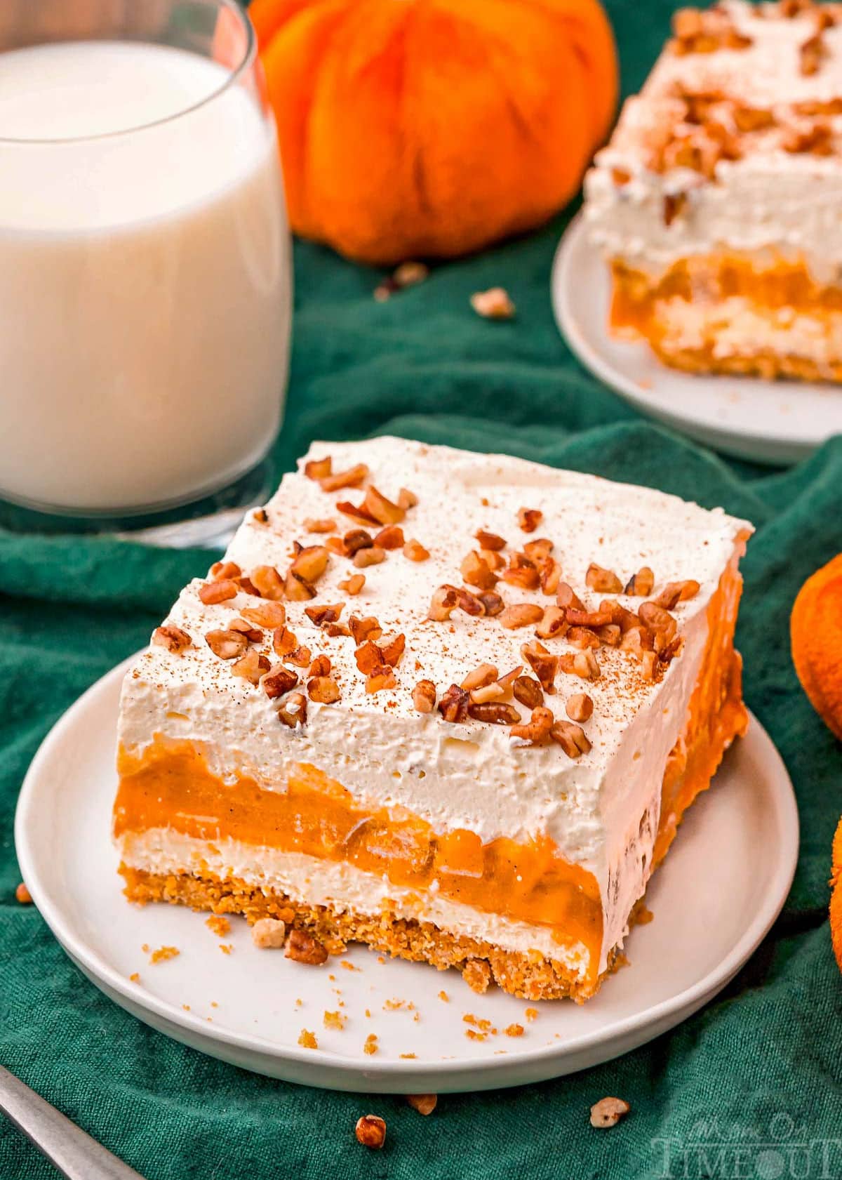 top down look at four layer pumpkin dessert sitting on white plate topped with pecans and pumpkin pie spice. glass of milk in background.