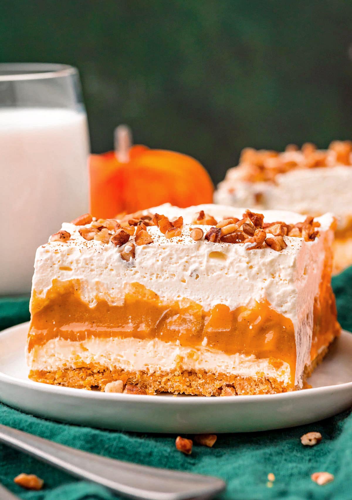 four layer pumpkin dessert sitting on white plate topped with pecans and pumpkin pie spice.