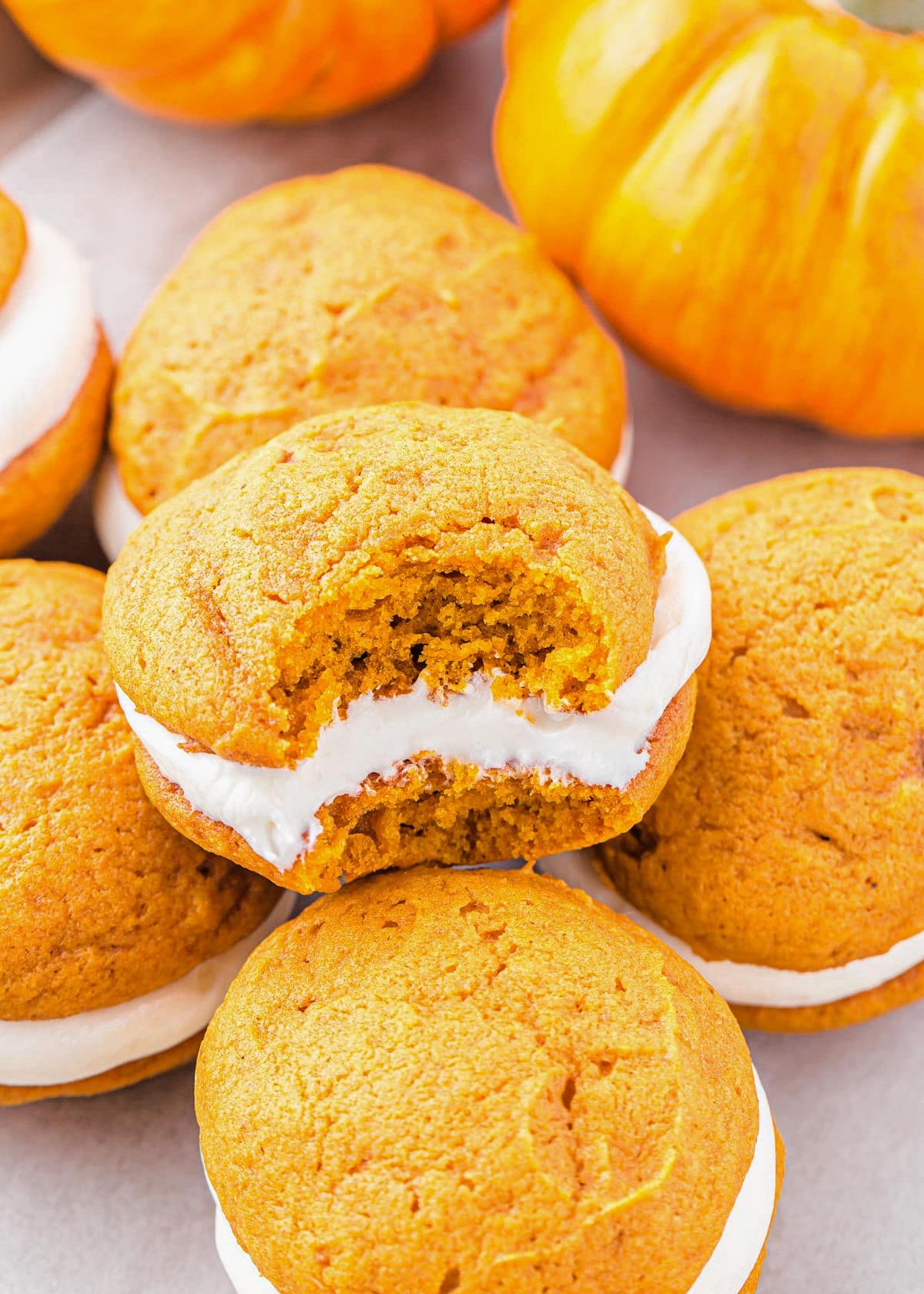 pumpkin whoopie pie with bite taken out of it sitting with more whoopie pies.