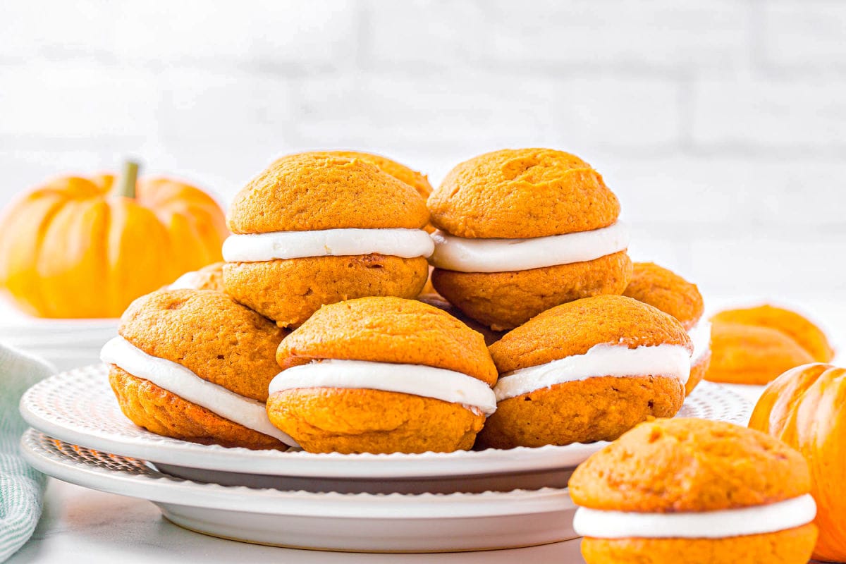 two white plates stacked with pumpkin whoopie pies piled on top.