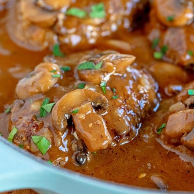 four salisbury steaks in large skillet with mushroom gravy and fresh parsley sprinkled over the top of them.