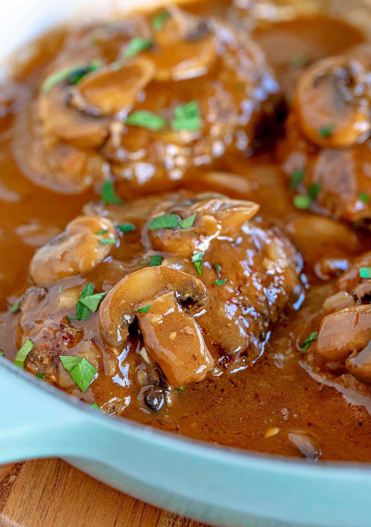 four salisbury steaks in large skillet with mushroom gravy and fresh parsley sprinkled over the top of them.