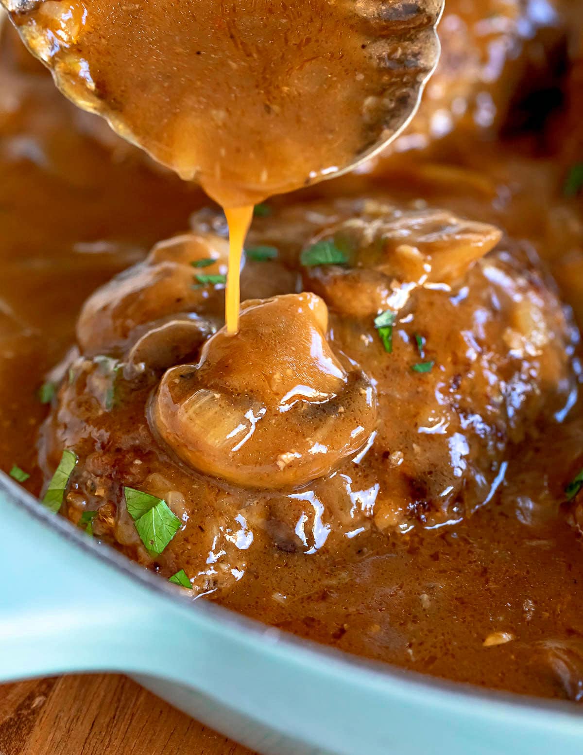 gravy being poured onto a salisbury steak still in the skillet.