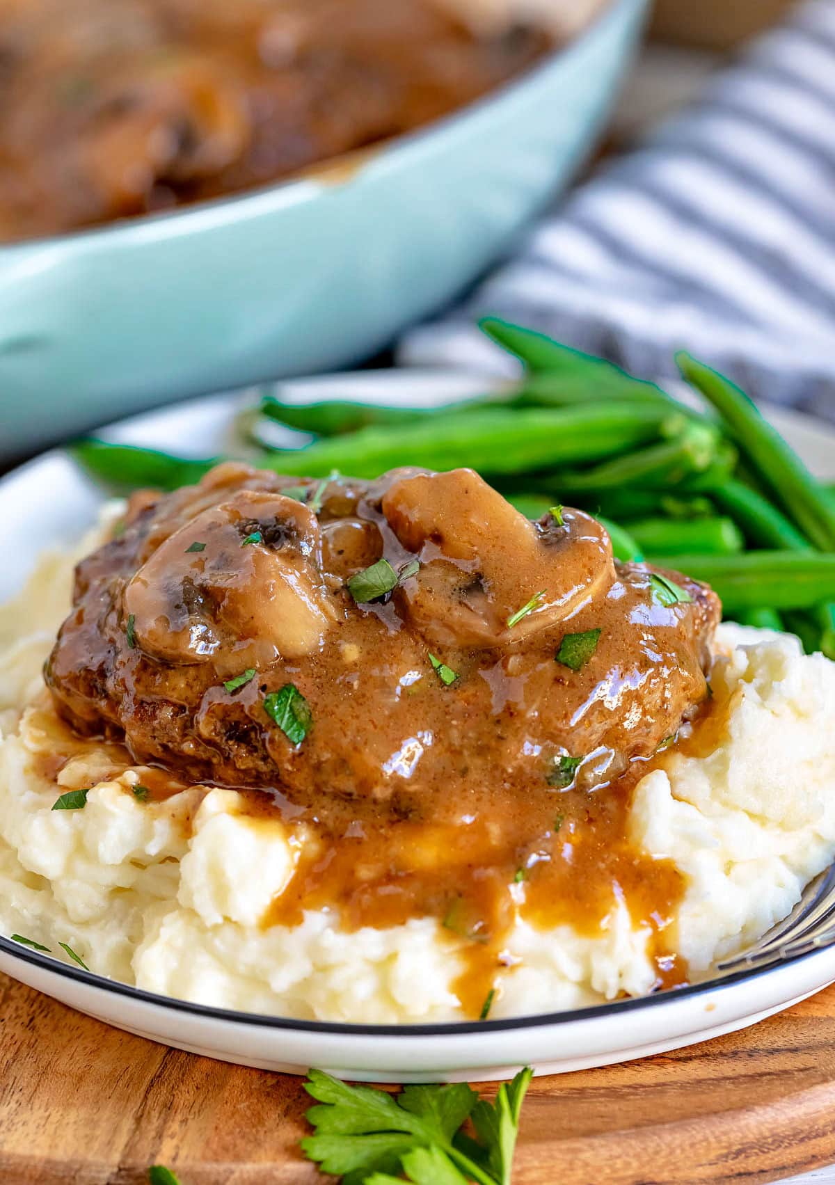 salisbury steak on bed of mashed potatoes with green beans as well. Mushroom gravy is drizzled on top of the steak and mashed potatoes.