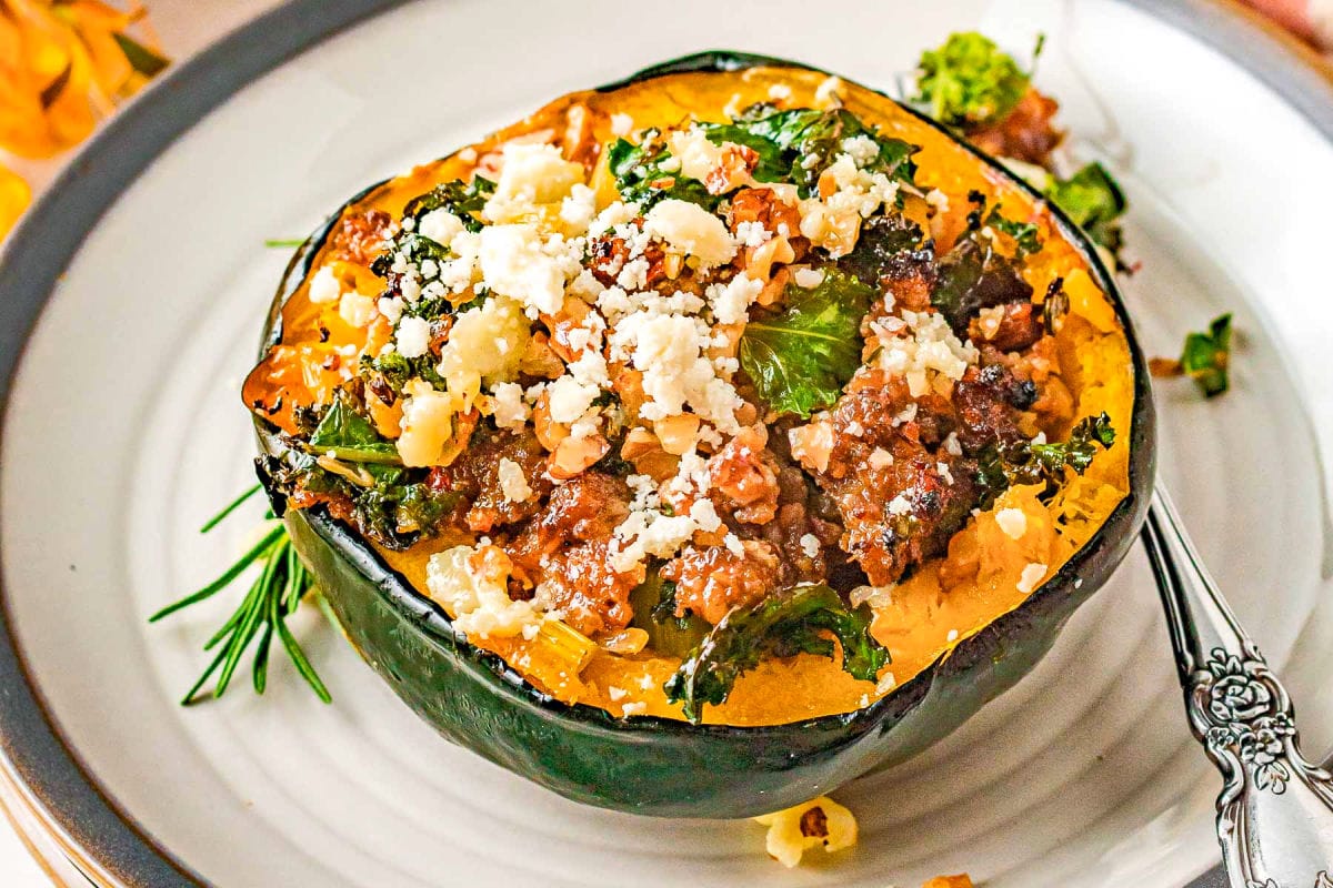 stuffed acorn squash on round white plate with gray edge topped with feta cheese and pecans.
