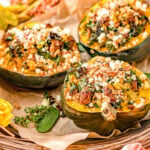 three stuffed acorn squash halves sitting on brown parchment paper topped with feta cheese.