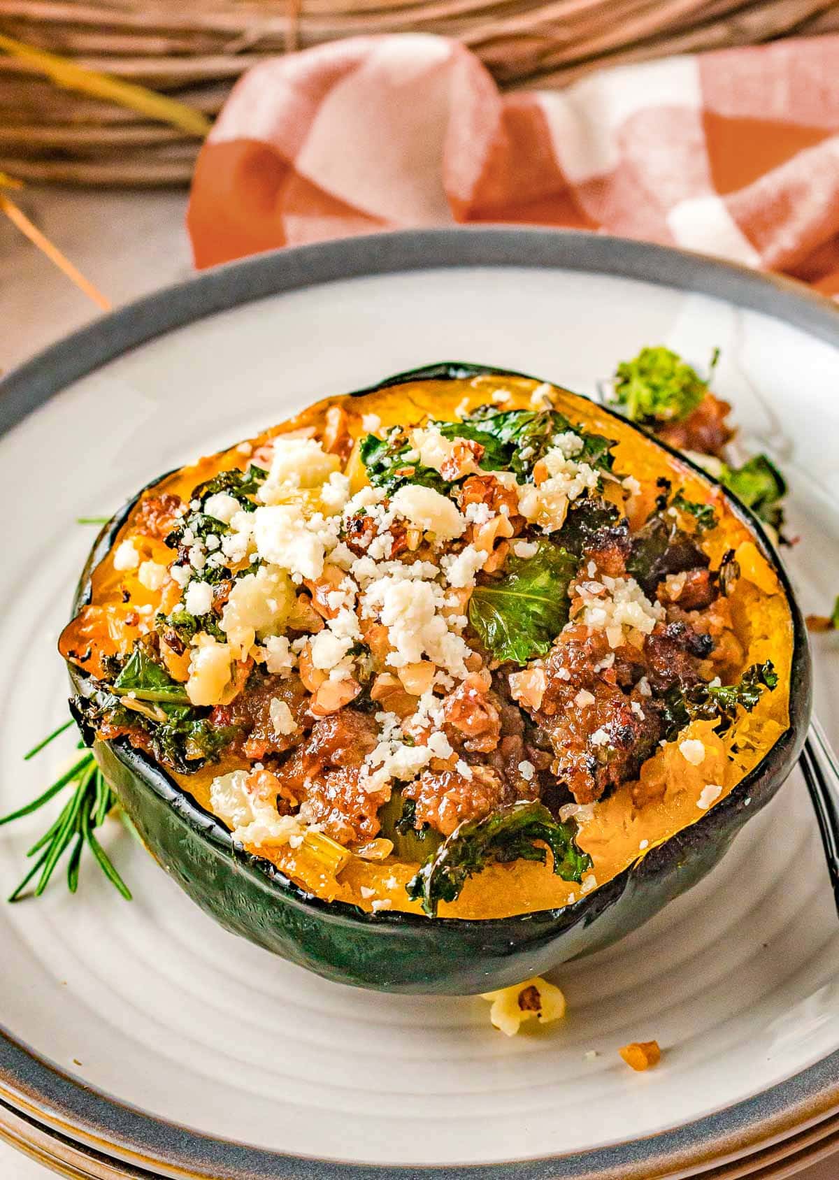 half of an acorn squash stuffed with sausage and veggies sitting on a white plate with a gray rim.