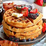 big stack of fluffy waffles topped with fresh berries butter and syrup.