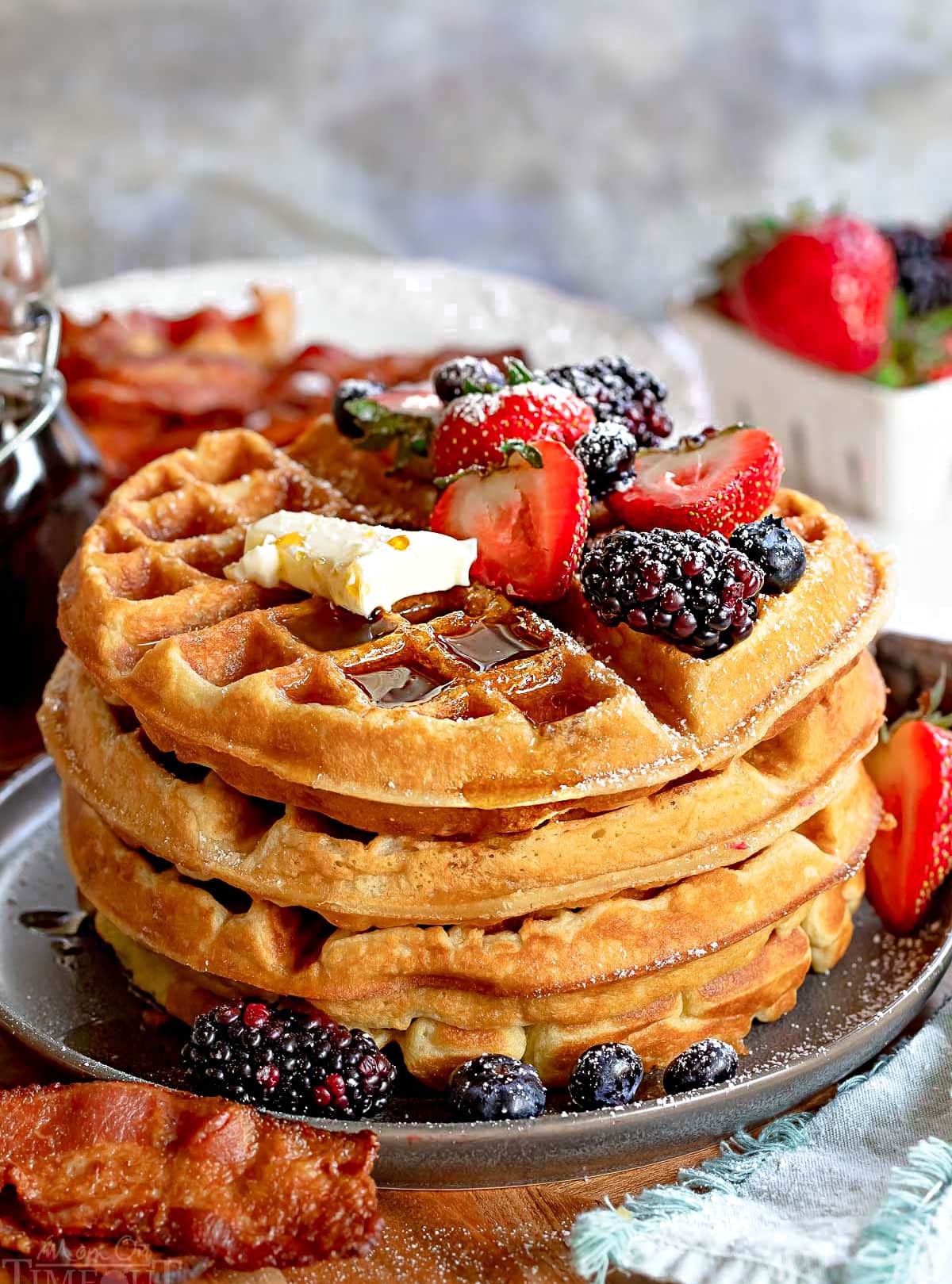 big stack of fluffy waffles topped with fresh berries butter and syrup. 