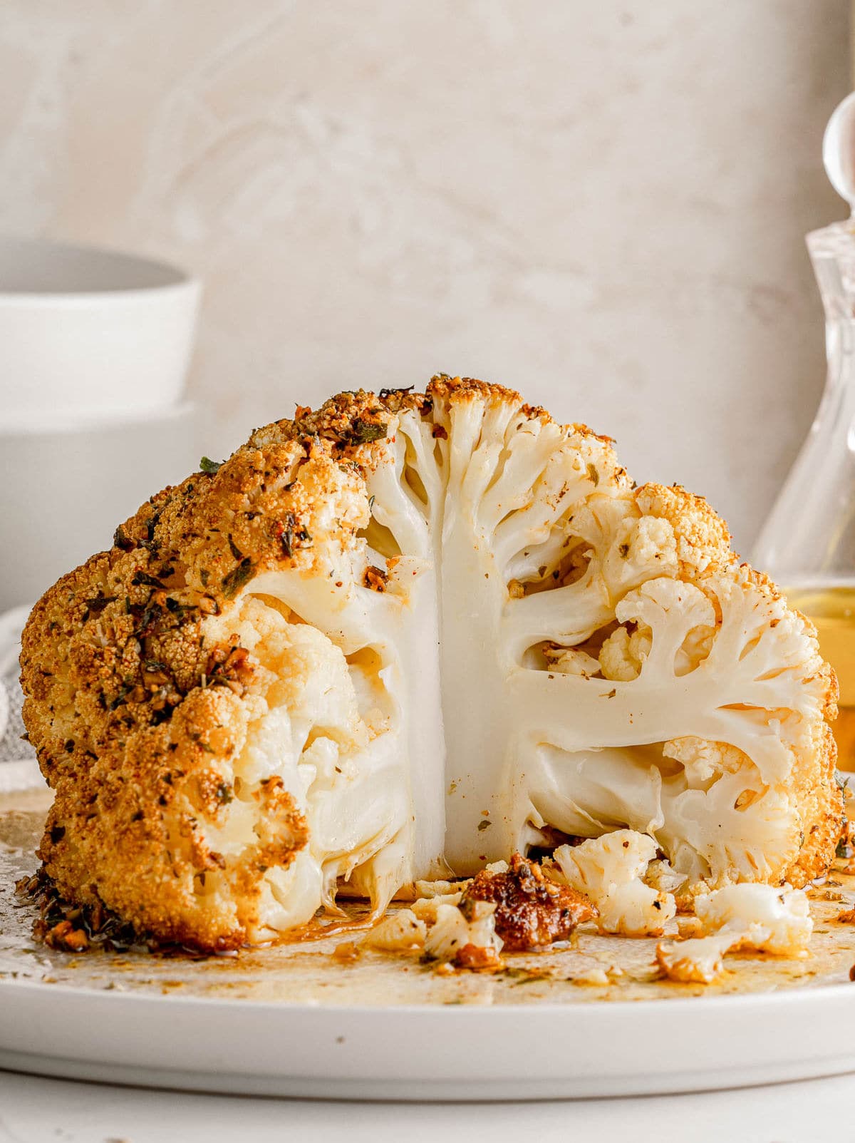 whole cauliflower head that has been seasoned and roasted in oven sitting on white plate with about one quarter of the head removed.