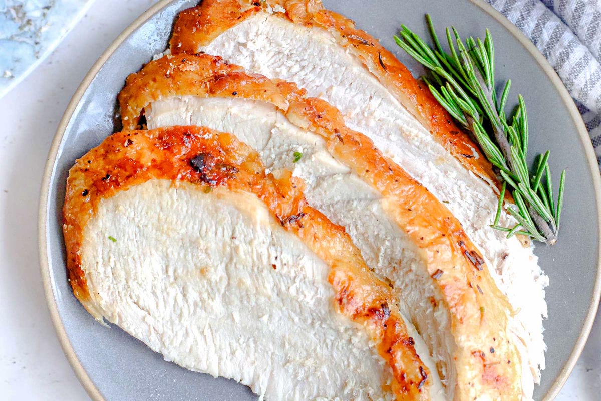 three slices of turkey breast sitting on plate with rosemary sprig to the side.