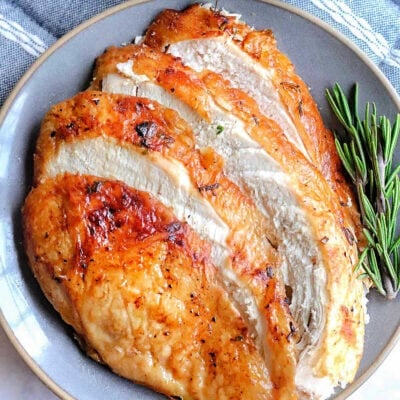 Slices of air fryer turkey breast fanned out on a gray plate next to a small bowl of mashed potatoes and gravy.