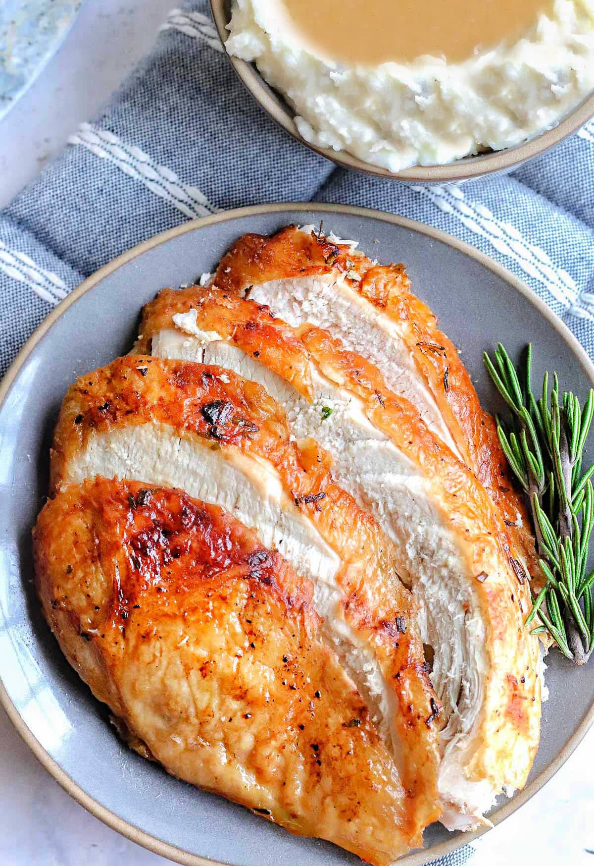 Slices of air fryer turkey breast fanned out on a gray plate next to a small bowl of mashed potatoes and gravy.