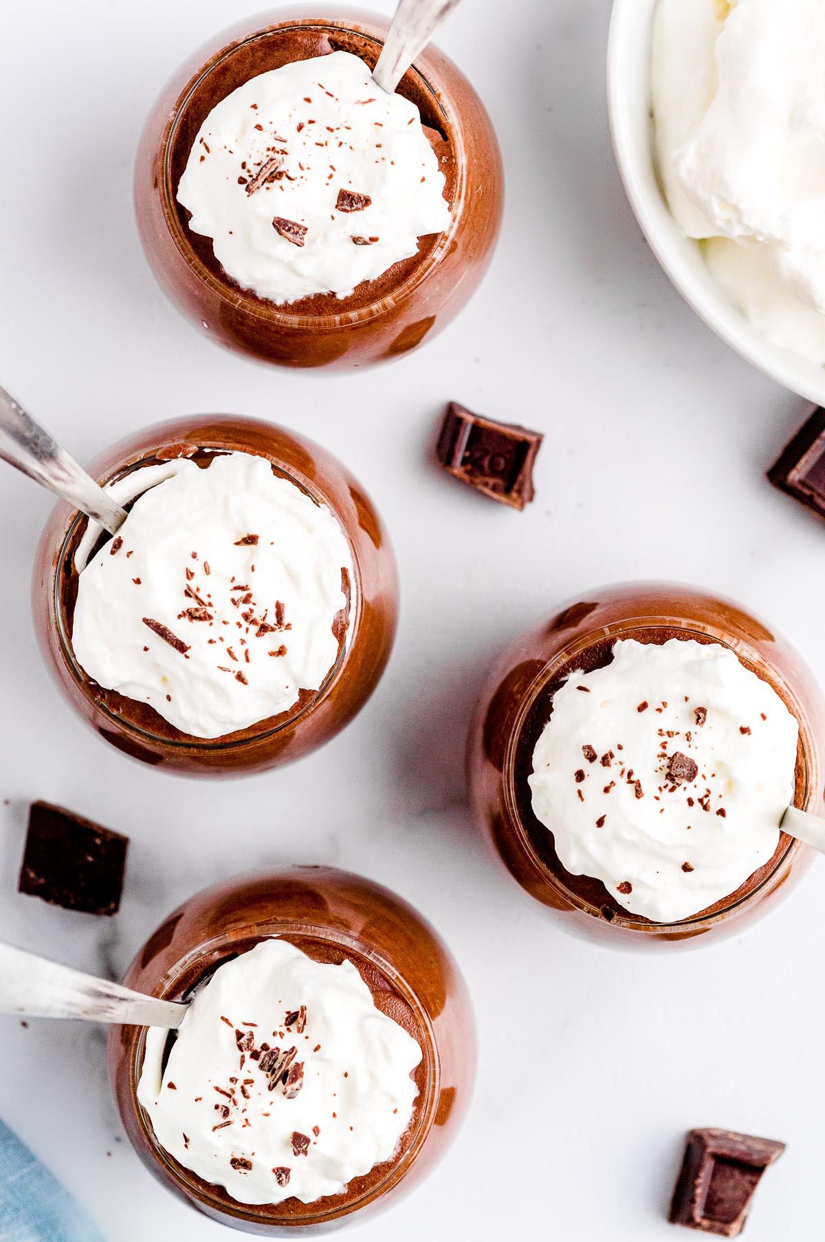 four glasses with chocolate mousse in them topped with whipped cream and chocolate shavings ready to be eaten.