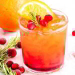 pretty crystal glass filled with christmas punch and garnished with rosemary, fresh cranberries and orange slice.