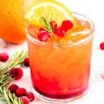 pretty crystal glass filled with christmas punch and garnished with rosemary, fresh cranberries and orange slice.