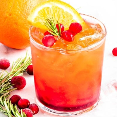 pretty crystal glass filled with christmas punch and garnished with rosemary, fresh cranberries and orange slice.
