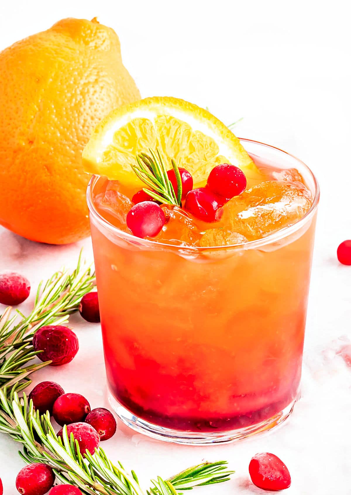 pretty crystal glass filled with christmas punch and garnished with rosemary, fresh cranberries and orange slice.