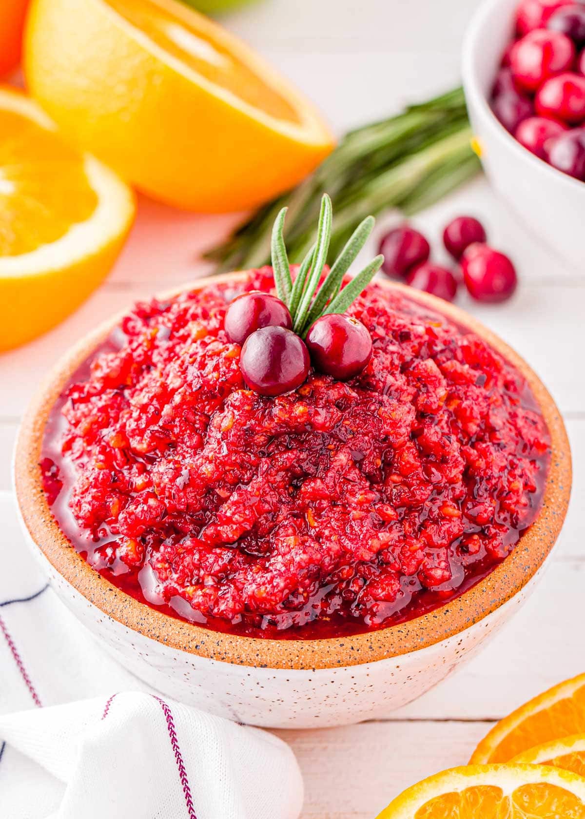 beautiful bowl of bright cranberry relish topped with a sprig of rosemary and three fresh cranberries.