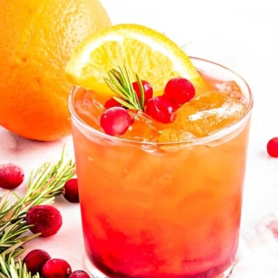 pretty crystal glass filled with christmas punch and garnished with rosemary, fresh cranberries and orange slice.