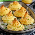 large brown tray with six duchess potatoes garnished with Parmesan cheese and snipped chives.